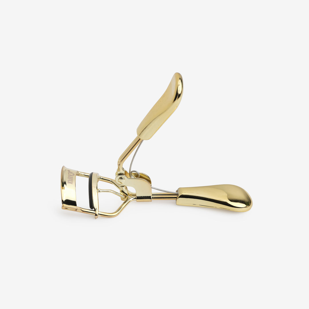 A gold-colored eyelash curler with a curved design and silicone rubber pad.