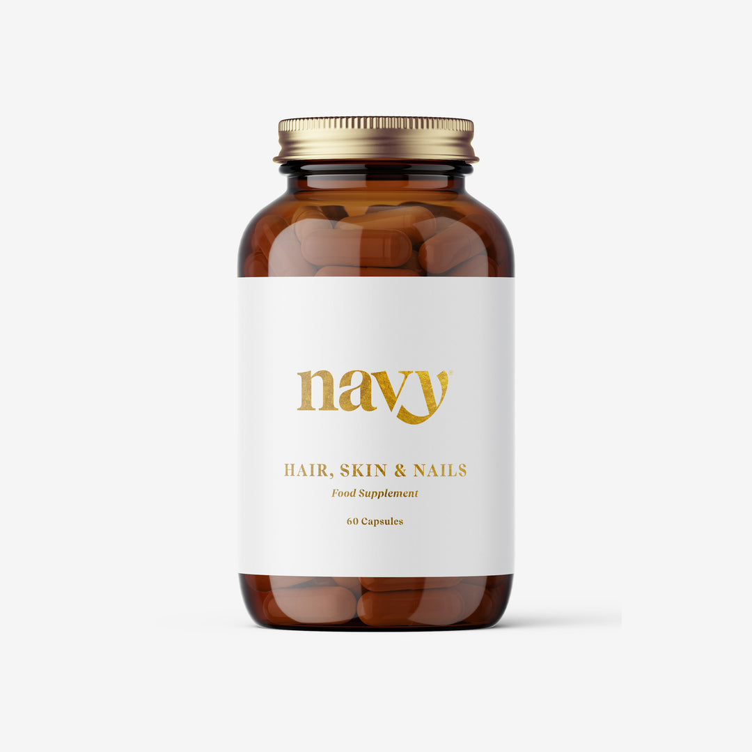A bottle of Navy Hair, Skin & Nails supplement with a white label and gold text on a clear glass container.
