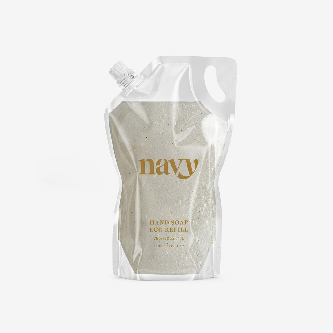 A clear pouch with navy branding containing navy exfoliating hand soap refill with visible fine pumice grains.