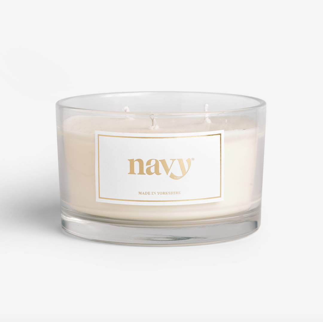 A triple-wick candle with a beige hue, housed in a clear glass jar with a label that reads 'navy'.