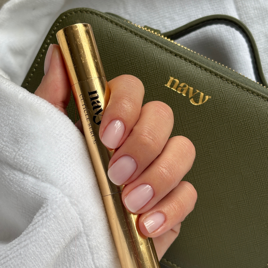Fresh delicate manicured nails holding a Navy Serum Pen in front of the Navy Country Green case. 