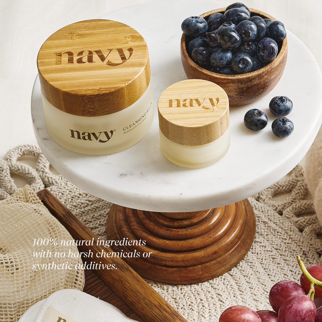 Two jars labeled 'navy' with wooden lids on a marble stand, surrounded by blueberries and grapes.
