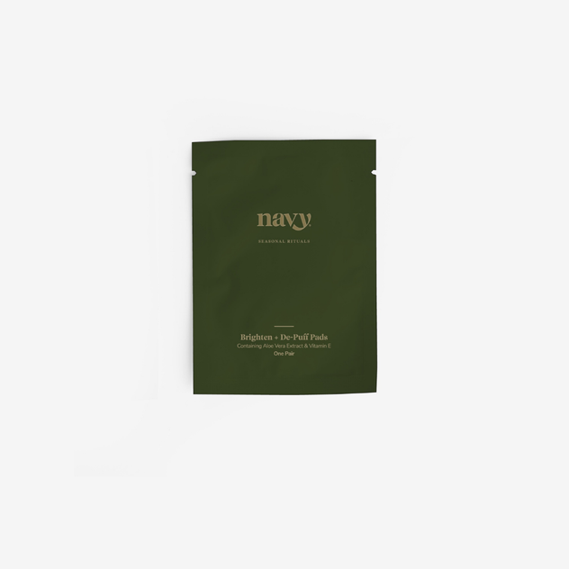 A dark green stand-up pouch of navy Cosmetics Brighten + De-Puff Pads on a clean white background.