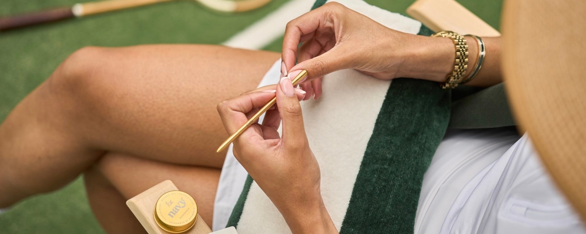 Person applying gold wax to a small container with a brush on a green surface.