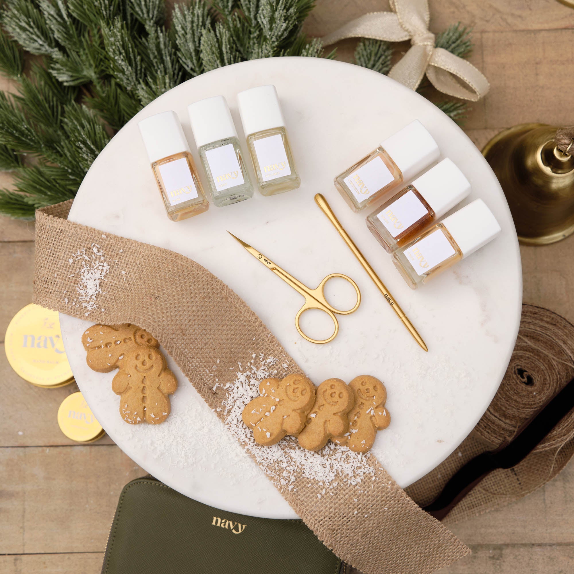 Nail polish bottles, scissors, and gingerbread cookies on a marble tray with decorative elements.