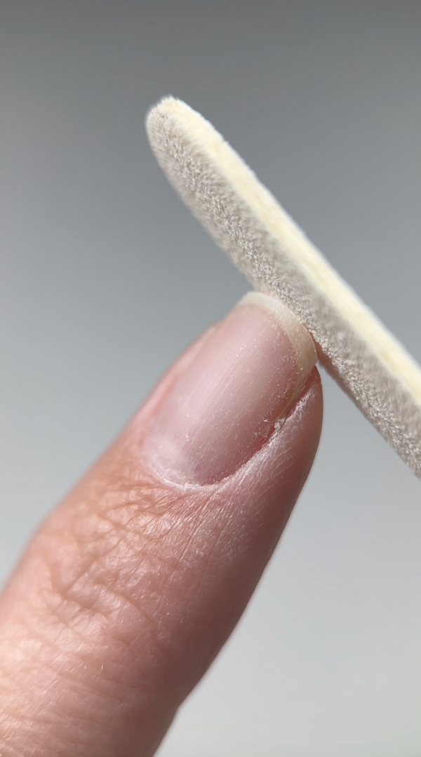 Close-up of a finger holding a small, cylindrical object against a neutral background