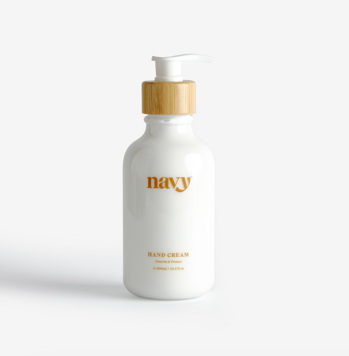 A pump bottle of Navy hand cream with a white label and a wooden pump, on a white background.