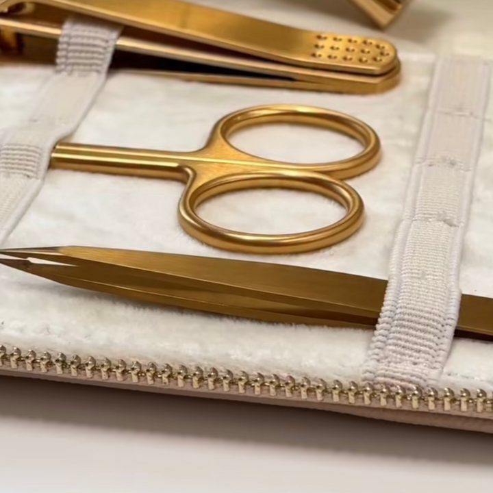Gold manicure set with scissors, clippers, and tweezers on a white background