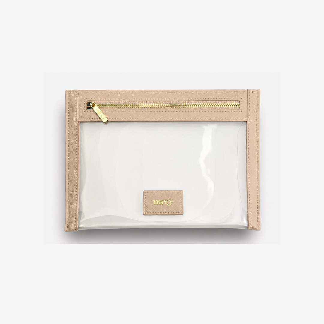 A clear plastic pouch with beige faux-leather trim and a gold zipper, featuring a small beige leather patch with the brand name 'navy' in gold lettering, set against a light gray background.