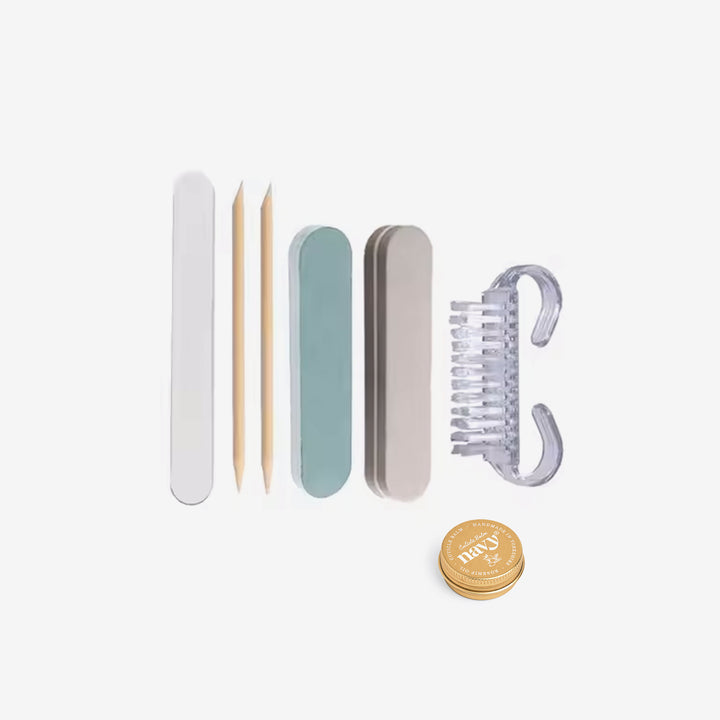 A collection of nail care tools including three nail files, a cuticle balm tin, orange wood sticks, and a reusable nail brush, presented in front of a white box with 'navy' branding.