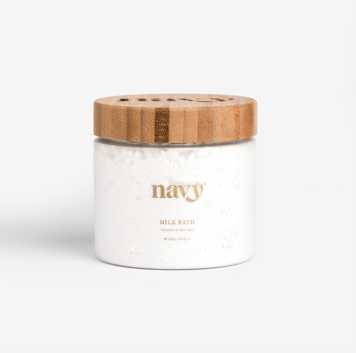 A container of Navy Milk Bath powder with a wooden lid, branded with the name 'Navy' on the front. A luxurious, 97% organic and vegan-friendly soak, 