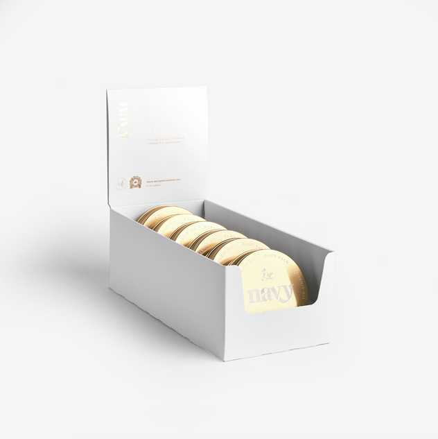 A white retail pack containing six gold-colored hand balm containers, displayed with an open lid and the brand name visible.