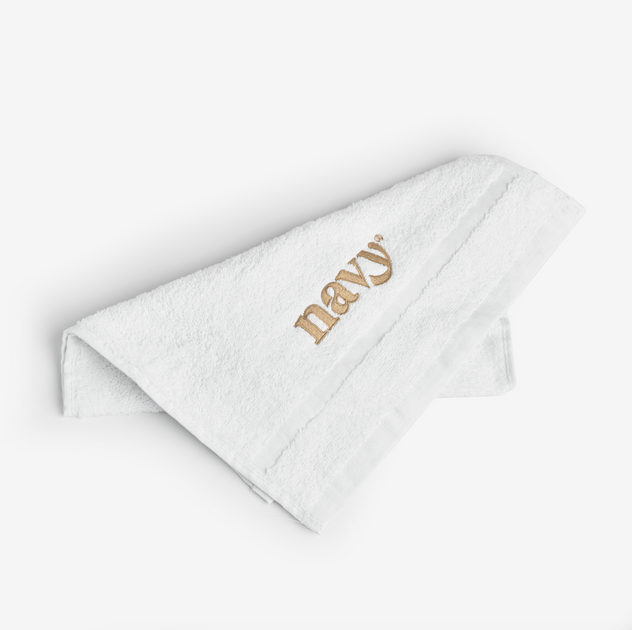 A folded white hand towel with the brand name 'Navy' embroidered in gold at the bottom.